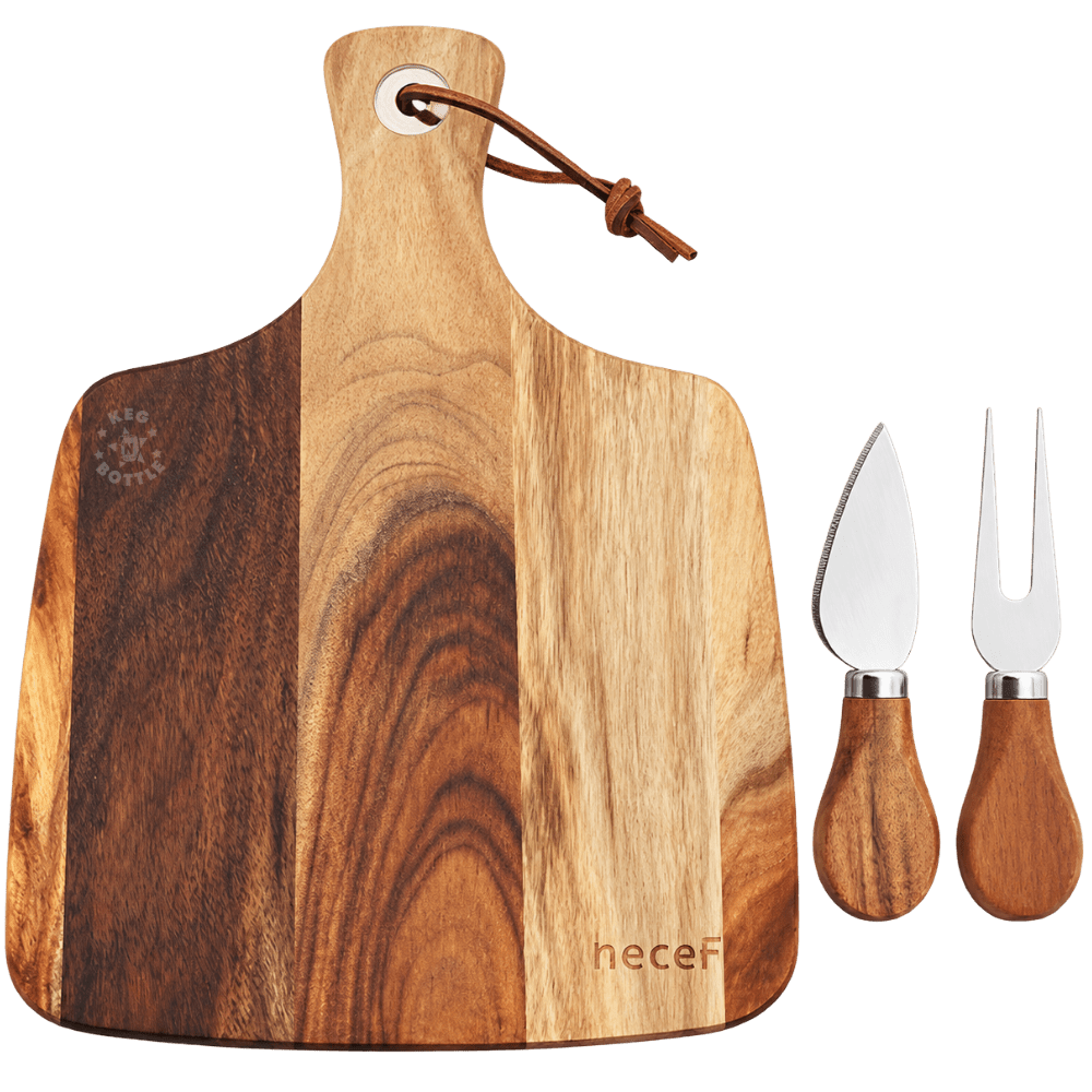 Natural acacia wood paddle-shaped charcuterie board with contrasting brown wood grain, leather hanging loop, stainless steel cheese knife, and matching two-prong serving fork with wooden handles.